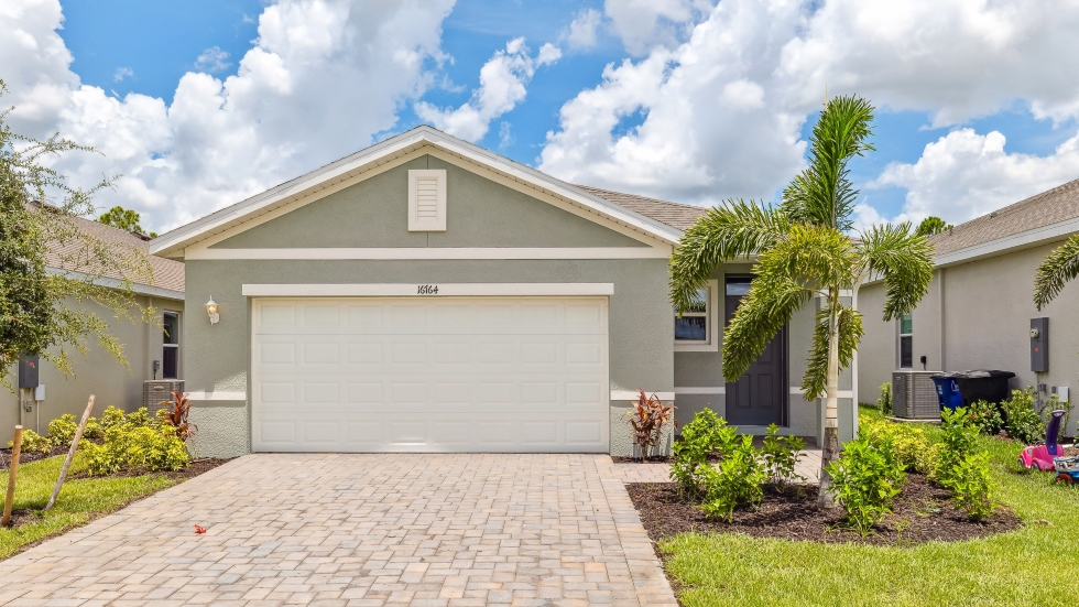 Outside of the Harper model C. Cream colored home with two car garage, window, and front door. Mixed paver driveway.