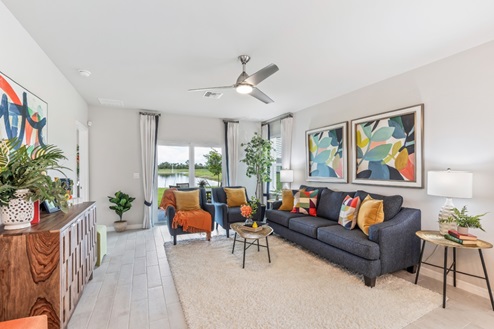 Inside of the Jemison model living room. Wood tile flooring and white walls. Room contains a couch, two armchairs, coffee table, side table, and dresser. In the background a sliding glass door leading to the back patio can be seen.