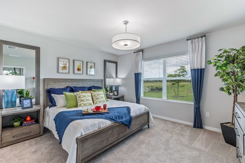 Inside of the Jemison model bedroom one. Grey carpet with off-white walls. Room contains one bed with nightstands on either side, a dresser on the opposing wall, and a plant in the corner of the room. Room also contains a window.