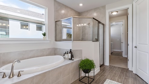 Inside of the Shelby model bathroom two. Wood floor tile and off-white walls. Bathroom contains a white tub with silver hardware as well as a shower with glass door and silver hardware. Bathroom connects to a walk-in closet.
