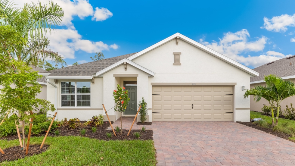 Outside of the Aria D model. Off-white home with two car garage, one large window with shutters, and front door. Mixed pavers driveway.