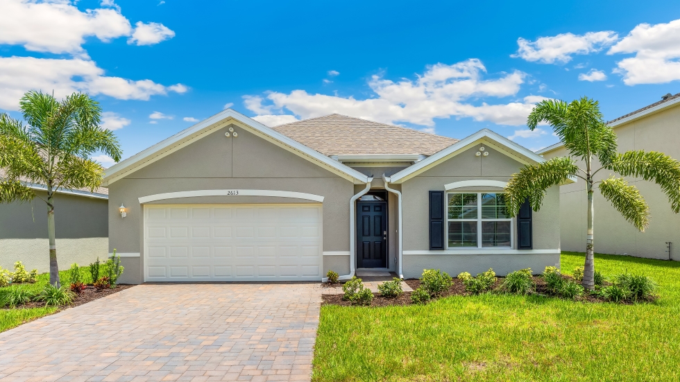 Outside of the Cali model C home. Blue home, two car garage, window with shutters, and front door. Mixed paver driveway.