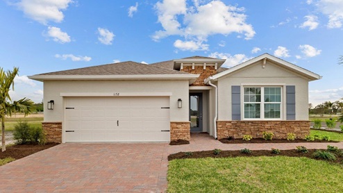 Outside of Delray model B. Yellow home with two car garage, one window with shutters, and front door. Mixed paver driveway.