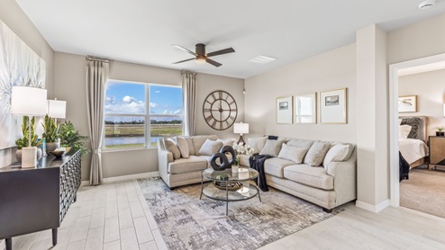 The Living room, there is a large white couch, a coffee table and a chest for storage. The room is well lit with a window overlooking a view of the back. You can see the entrance to the Master bedroom from here.