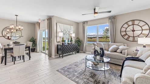 The wooden dining table is set for a family of six. There is a chandelier on top and a mirror on the wall behind. The Dining space is well lit from the patio doors. There are curtains on either side of the patio doors. You can also see the living room from here