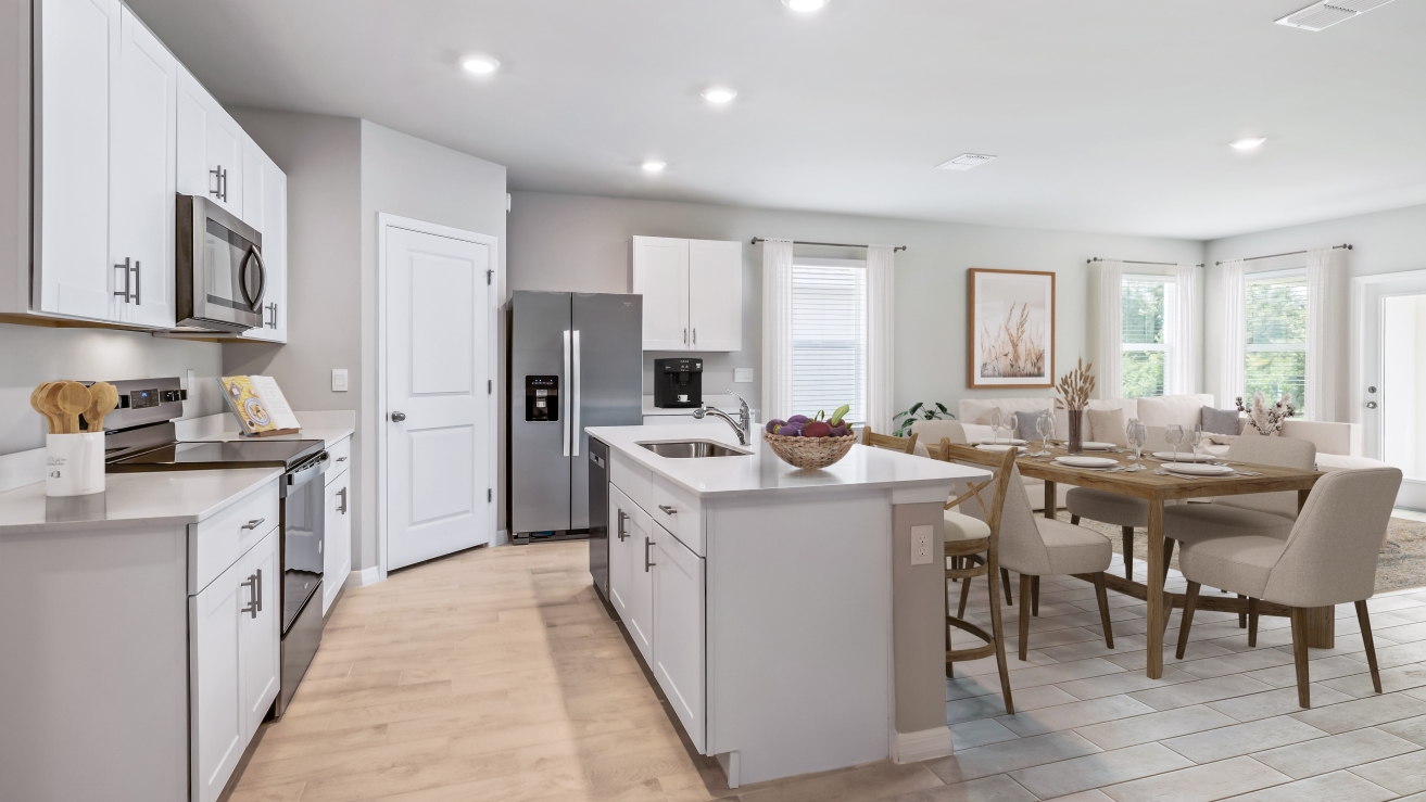 Inside the Lakeside kitchen which shows stainless steel appliances and white cabinetry with rattan stools at the bar for sitting. You can see the dining room table and part of the living room from this angle.