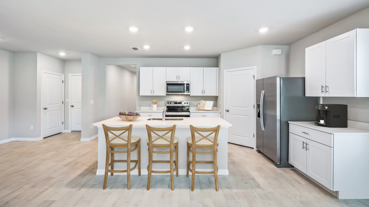 Inside the Lakeside kitchen which shows stainless steel appliances and white cabinetry with rattan stools at the bar for sitting.