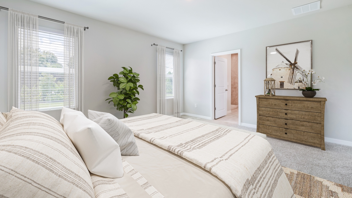 Inside the fifth bedroom of the Lakeside. Carpetted floors and gray walls with Farmhouse style décor. There is a window for viewing the landscaped area outside. View point is from the bed into the bathroom across the way.