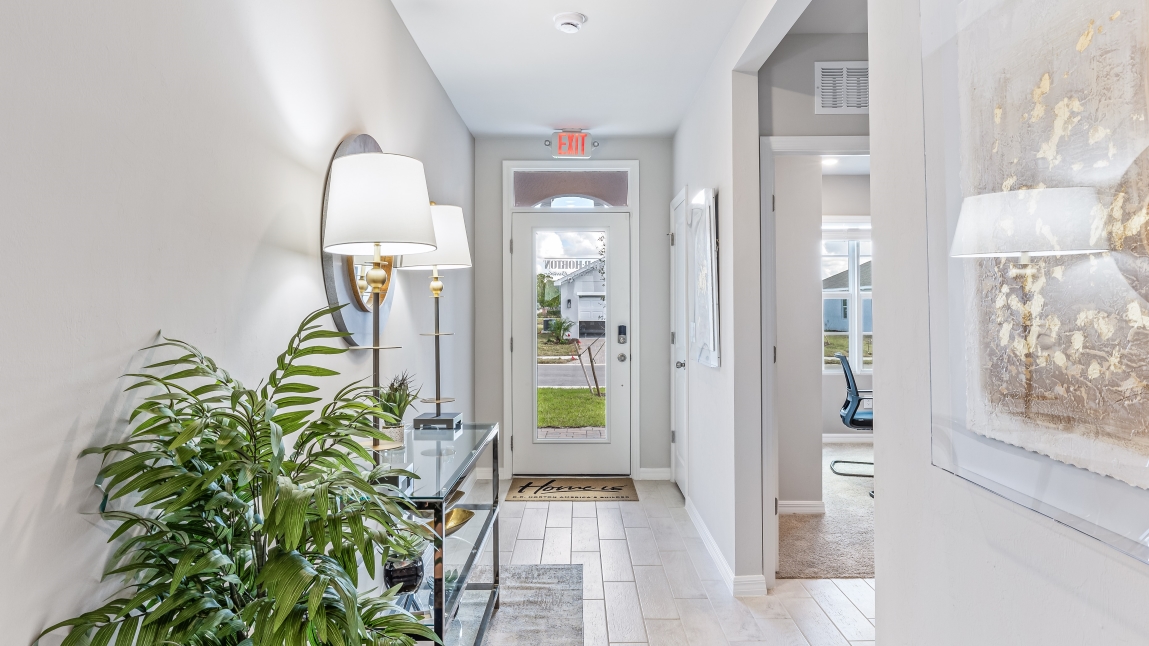 Inside of the Cali model hallway. Tile flooring, off-white walls. Hallway to the front door and den area.