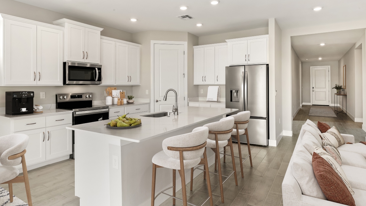 Inside of the Shelby model home kitchen with stainless steel appliances and a bar with stools for sitting.