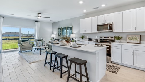 The kitchen has modern solid white cabinetry and stainless steel appliances. There is bar seating. You can see the back view of the townhome with the sliding doors. You can see an angle of the living room from here as well.