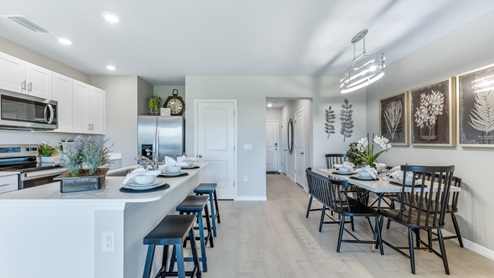 The kitchen has modern solid white cabinetry and stainless steel appliances. There is a pantry and bar seating. You can see the front door from this angle. This also shows the Bayside's dining area, its right after the entrance to the townhome. It can seat up to 6 people and is across from the kitchen/bar.