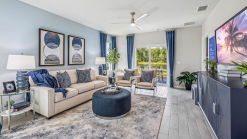 Inside of the Jemison model living room. Wood tile flooring and white walls. Room contains a couch, two armchairs, coffee table, side table, and dresser. In the background a sliding glass door leading to the back patio can be seen.