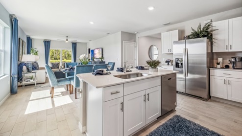 Inside of the Jemison model kitchen. Wood tile floors and white walls. Kitchen contains white countertops and cabinets with silver hardware. Kitchen also has a kitchen island with bar-style seating.