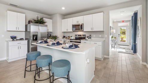 Inside of the Jemison model kitchen. Wood tile floors and white walls. Kitchen contains white countertops and cabinets with silver hardware. Kitchen also has a kitchen island with bar-style seating.