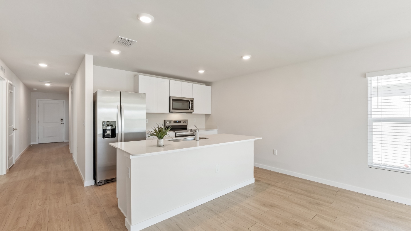 Inside of the Cameron B model kitchen. Revwood floors, white walls, white cabinets, with stainless steel appliances.