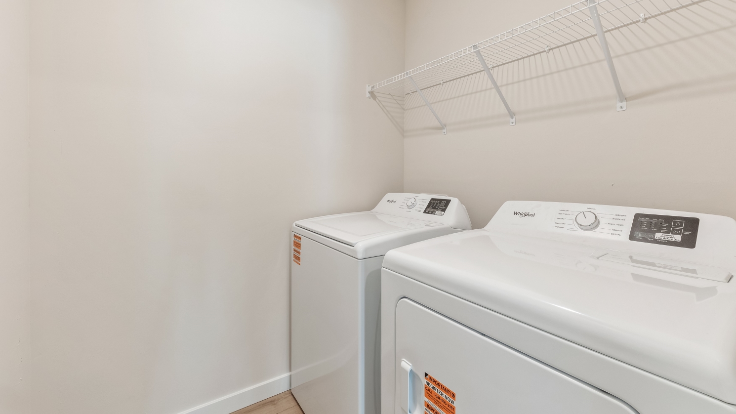 Inside of the Cameron B model laundry room. Washer and dryer with shelves above.