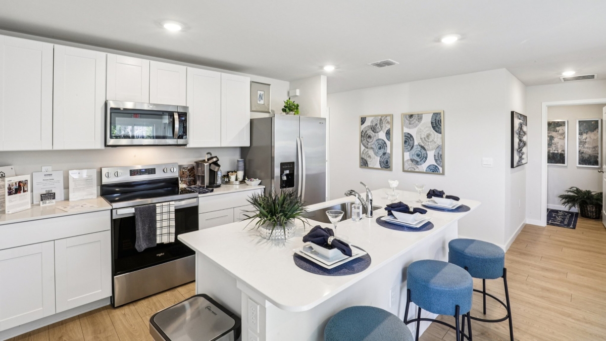 Inside of the Cameron B model kitchen. Revwood floors, white walls, white cabinets, with stainless steel appliances.