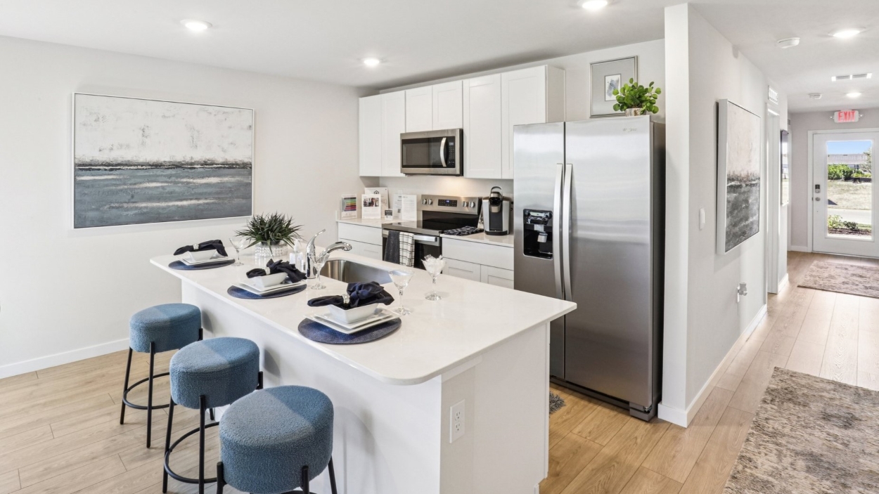 Inside the Cameron model kitchen. White counter tops and white cabinets, with stainless steel appliances.