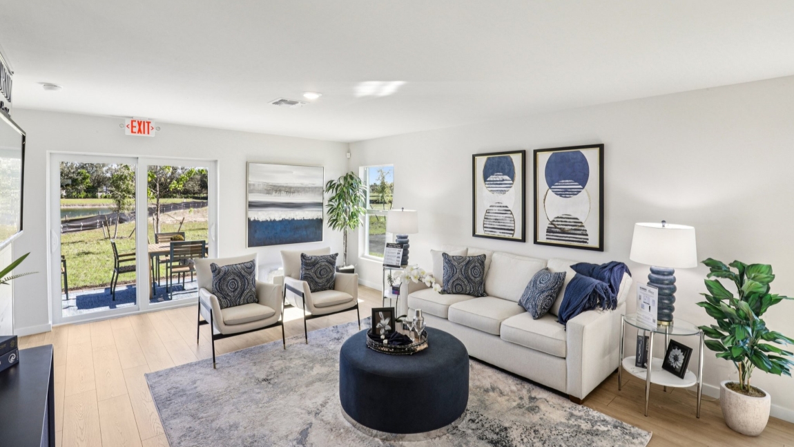 Inside the living room of the Cameron model. RevWood floors with white walls. Small couch, two side chairs, and ottoman.