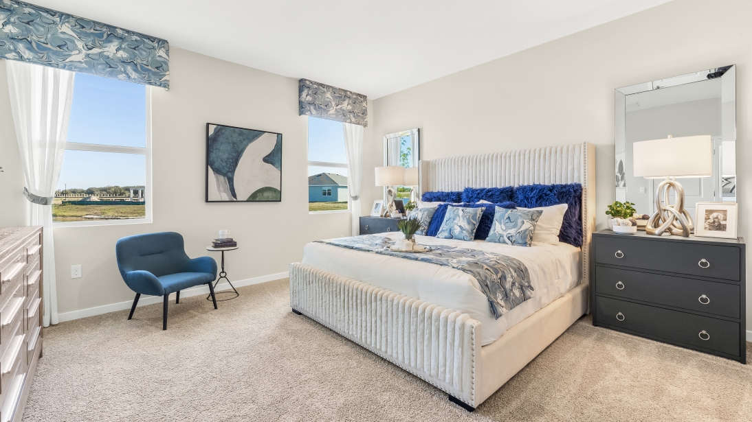 Inside the Lantana model bedroom 3. Contains a bed with a dresser next to and across from it. Also contains a side table and three windows.