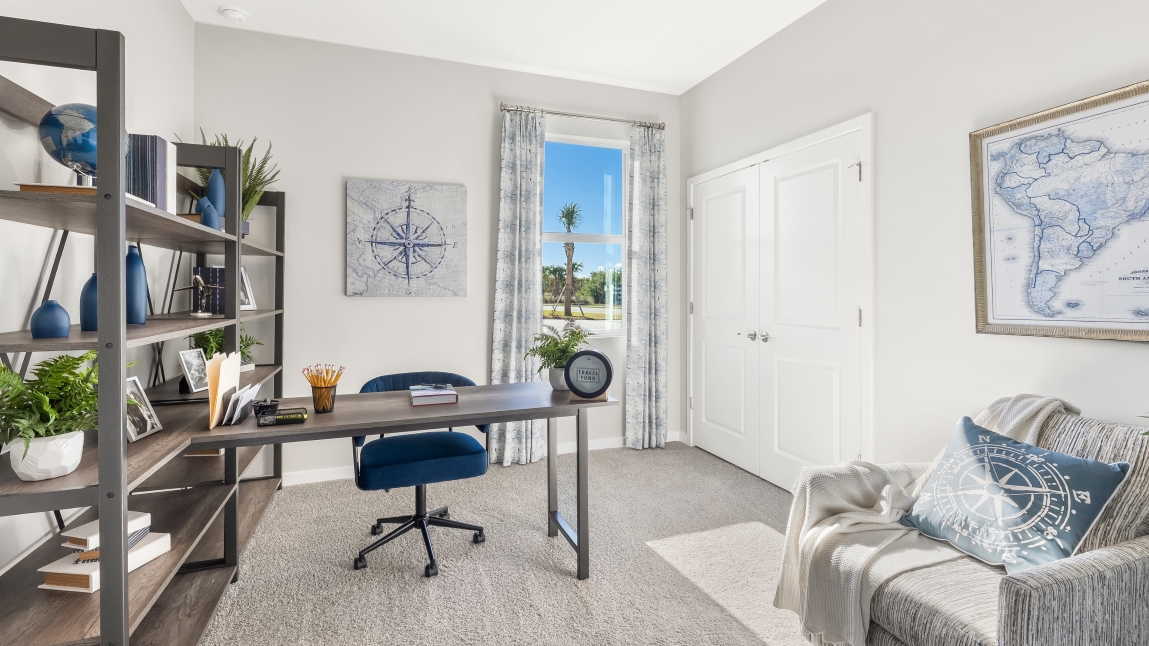 Inside the Lantana model den. Includes shelves with knick knacks and storage space. As well as a desk with a desk chair, and a side chair in the corner.