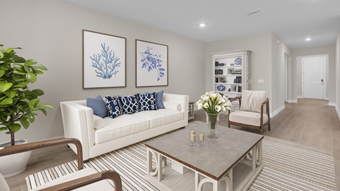 Inside of the Delray B model living area. Wood tile floors and off-white walls. Room contains a couch, two armchairs, coffee table, and storage shelf with nick-nacks.