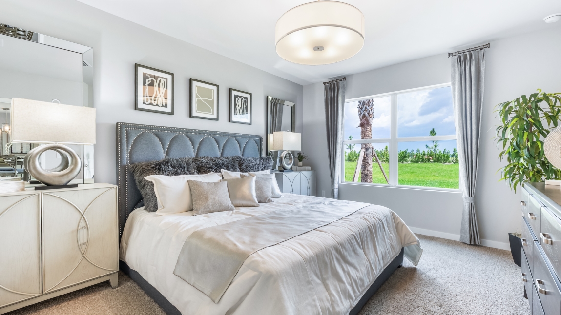 Inside of the Cali model bedroom one. Creme carpet with grey walls. Room contains a large bed with dressers on either side.
