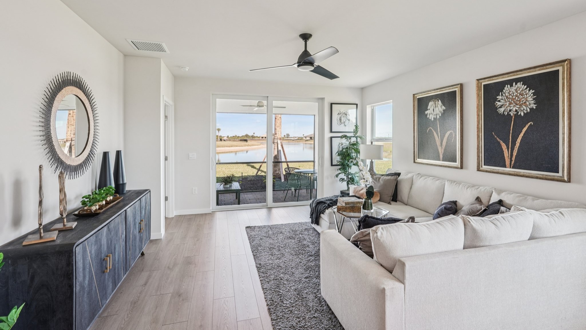 Inside the Carrington model living room. Revwood floors and off-white walls. Large couch and a TV stand table. Room connects to the outdoor patio area.