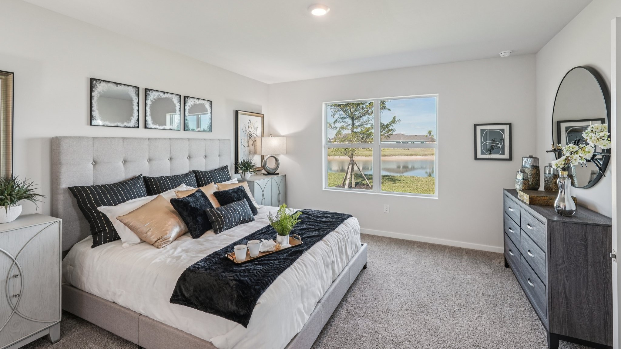 Inside bedroom 2 of the Carrington model. Large bed with side tables on either side and a dresser across from the bed. Room contains a window.