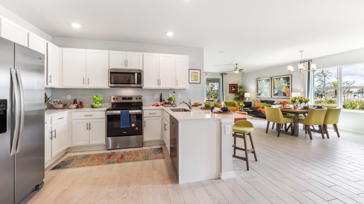 Kitchen with white cabinets, stainless steel appliances, and a peninsulta for bar-style eating. Dining area are living room can be seen.