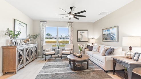 The Living room, there is a large white couch, a coffee table and a chest for storage. The room is well lit with a window overlooking a view of the back.