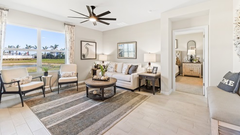 The Living room, there is a large white couch, a coffee table and a chest for storage. The room is well lit with a window overlooking a view of the back. You can see the entrance to the Master bedroom from here.