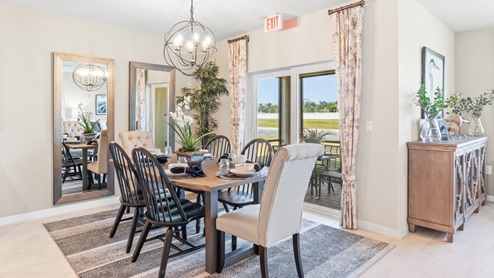 The wooden dining table is set for a family of six. There is a chandelier on top and a mirror on the wall behind. The Dining space is well lit from the patio doors. There are curtains on either side of the patio doors.