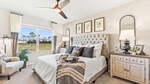 The third Bedroom is carpeted with grey painted walls. There is a window with a view of the back of the home. There are side tables on either side of the freshly made bed. There is a chandelier above the bed as well. Here you can see the dresser for clothes across from the bed and the plant in the corner.