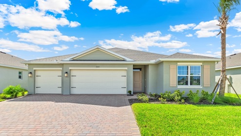 Outside the Covington G model. Beige home with three car garage, blue door, a window with decorative shutters, and mixed paver driveway.