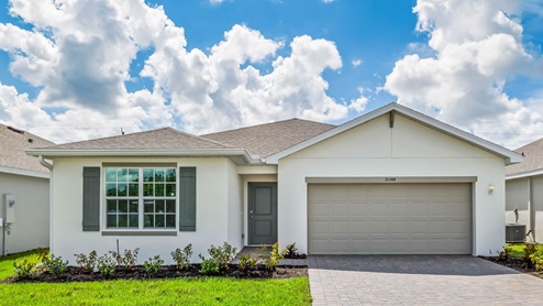 Exterior elevation of green home with white trim, tan doors and shutters, with tan paver driveway.