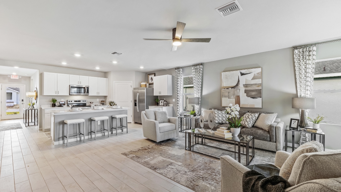 Inside the Lakeside Model Living room and Kitchen. You can see the front door from here. Floor is tiled and walls are painted grey. All silver/neutral furnishings.