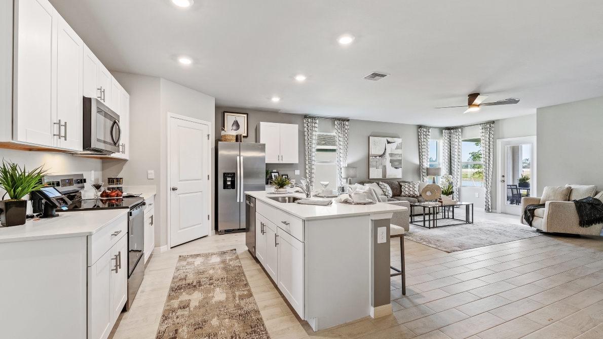 Inside the Lakeside Model Living room and Kitchen. You can see the patio door from here. Floor is tiled and walls are painted grey. All silver/neutral furnishings. The Kitchen is well equipped with all stainless-steal appliances