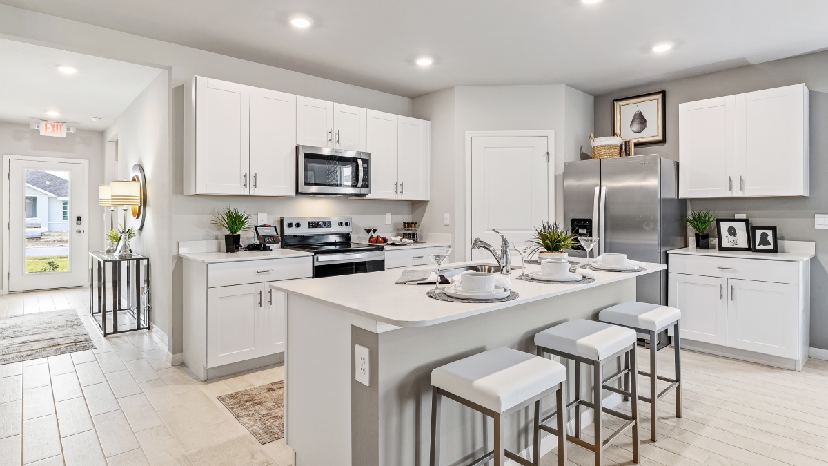 Inside the Lakeside Model Kitchen. You can see the front door from here. Floor is tiled and walls are painted grey. All silver/neutral furnishings. The Kitchen is well equipped with all stainless-steal appliances. There are stools for Bar seating