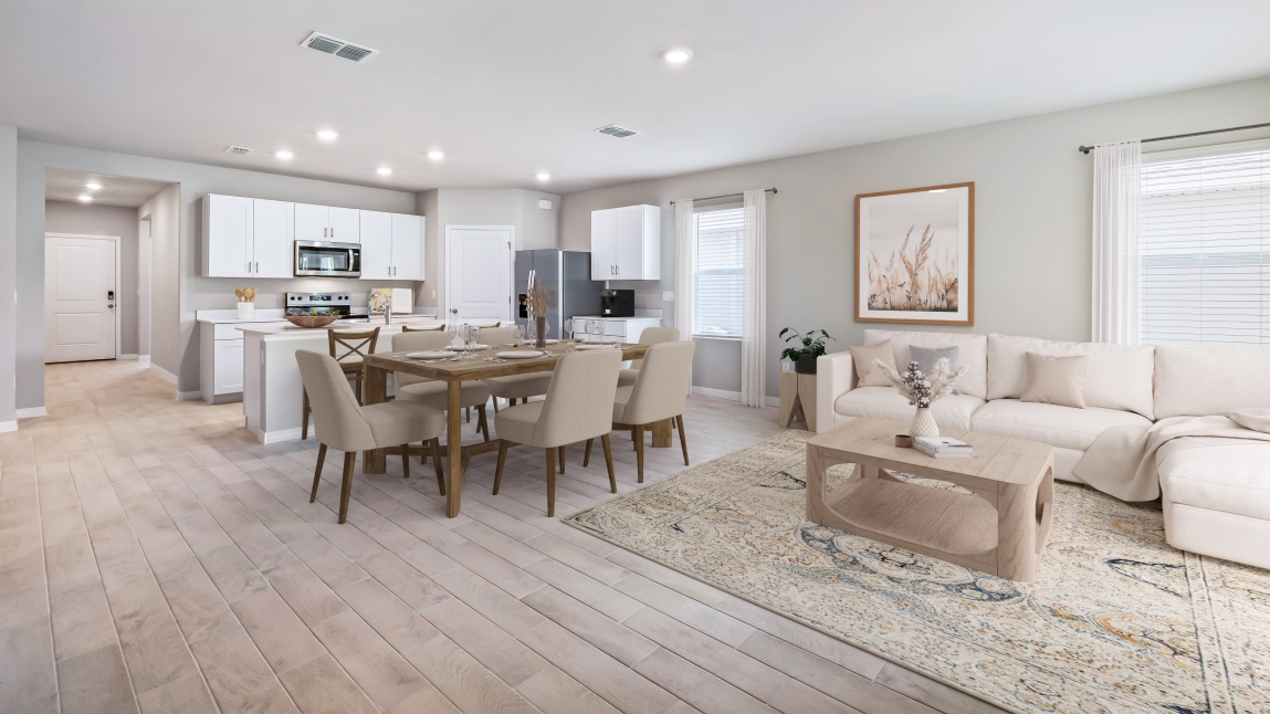 Inside the Lakeside kitchen and dining room with view of the living room. Kitchen shows stainless steel appliances and white cabinetry with rattan stools at the bar for sitting. Dining table is wooden with plushed seating for 6 people. Living room couch is white and furniture is all wood.