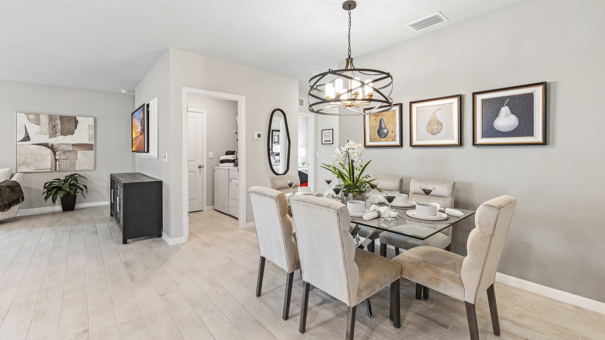 Inside the Lakeside Model Dining Area. You can see the laundry room and living room from here. Floor is tiled and walls are painted grey. All silver/neutral furnishings. The area can fit up to 6 people and there is a bathroom nearby.