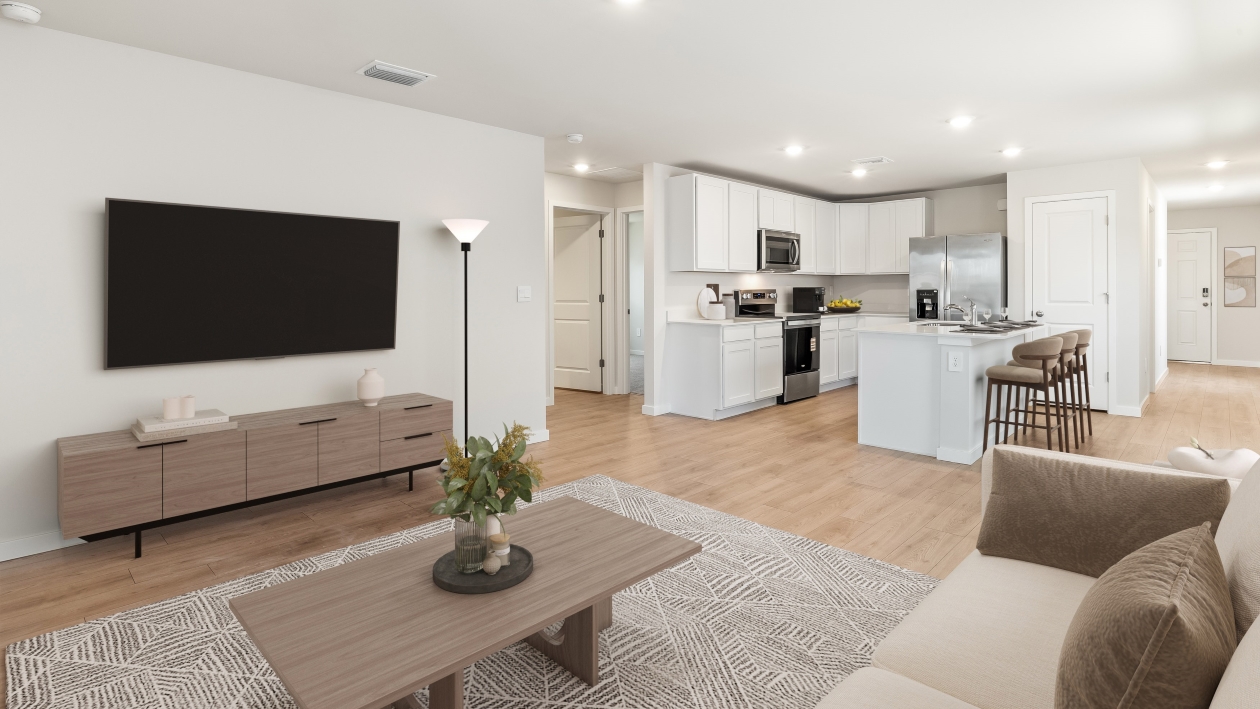 Inside the Downing model living room. Revwood floors with white walls. Couch, coffee table, TV, and TV stand. You can see the kitchen in the back.