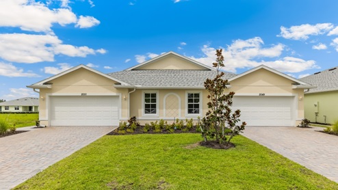 Outside of the Carrington model. Yellow home with two windows, two garages, two front doors. Two grey paver driveways. Side angle