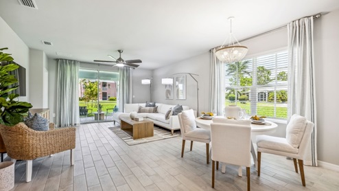 Inside of the Carrington model. Wood tile flooring with off-white walls. Room contains a couch, an armchair, coffee table, and small side table. Dining room can be seen in the background. You can see the patio from this angle.