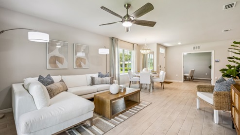 Inside of the Carrington model. Wood tile flooring with off-white walls. Room contains a couch, an armchair, coffee table, and small side table. Dining room can be seen in the background.