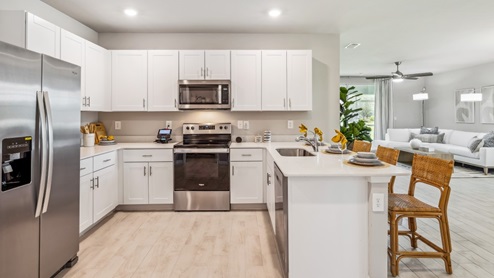 Inside of the Carrington model. Wood tile flooring with white countertops and cabinets with silver hardware. Kitchen island with bar-style seating and stainless-steel appliances. Appliance angle