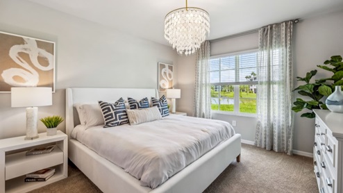 Inside of the Carrington model bedroom one. Crème carpets and off-white walls. Room contains bed with nightstands on either side as well as a dresser. Room also has window.