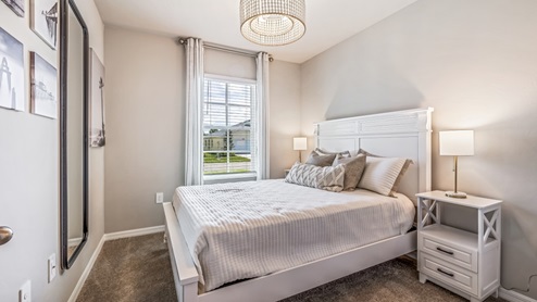 Inside of the Carrington model bedroom two. Crème carpets and off-white walls. Room contains bed with nightstands on either side as well as a dresser. Room also has window.