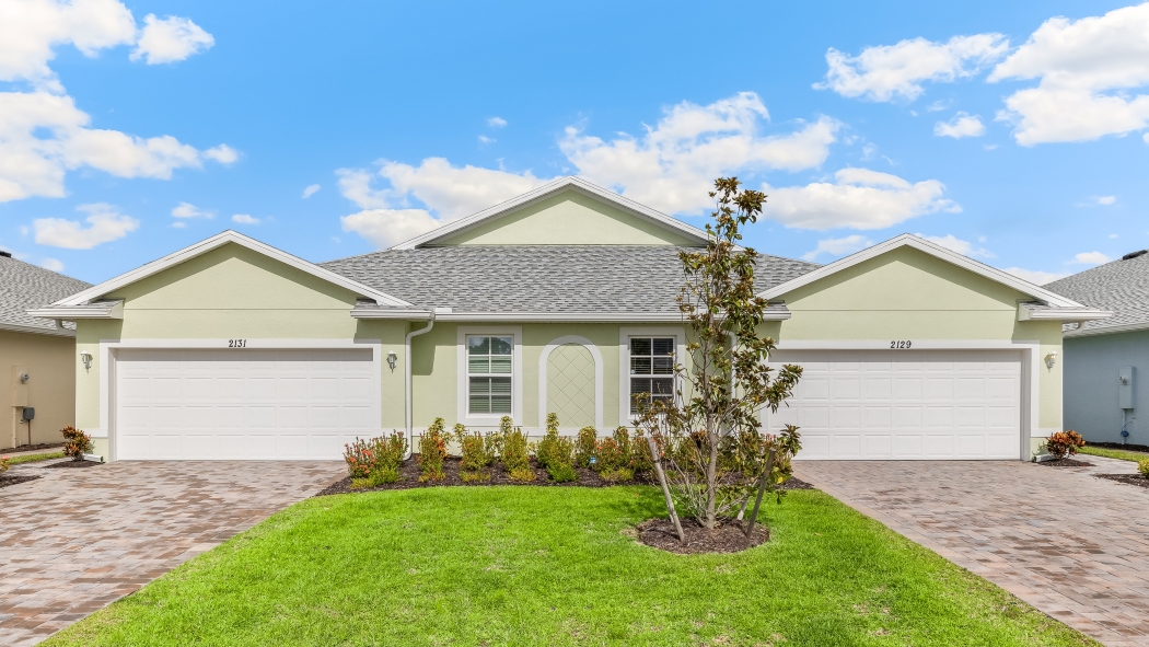 Outside of the Carrington model. Green home with two windows, two garages, two front doors. Two grey paver driveways.